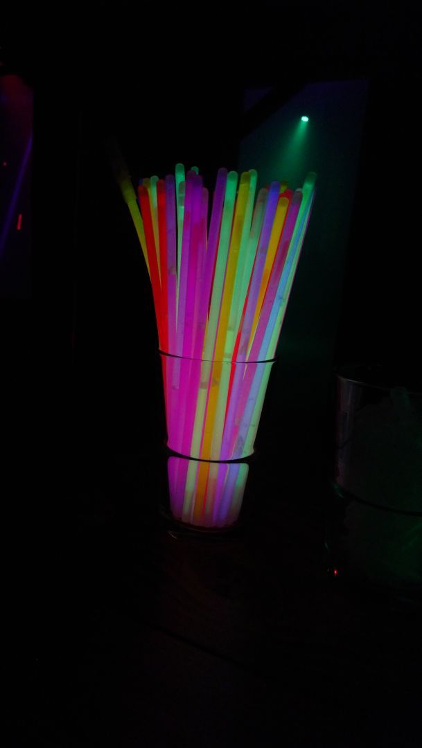 Ein Glas voll bunter Plastik-Strohhalme die in Schwarzlicht leuchten