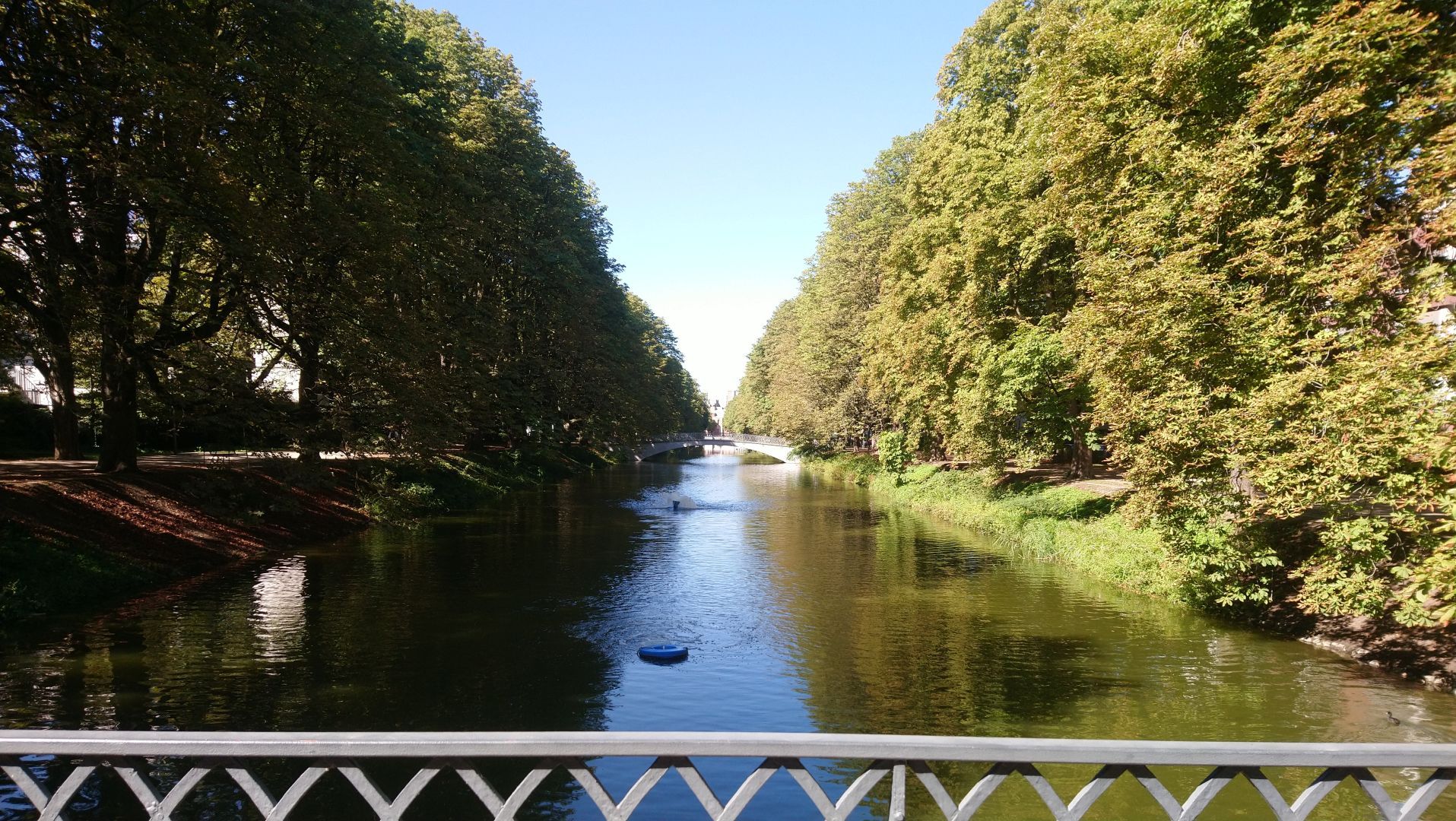 Blick von einer niedrigen Brücke auf einen geraden Fluss/Kanal umgeben von dichten grünen Bäumen links und rechts
