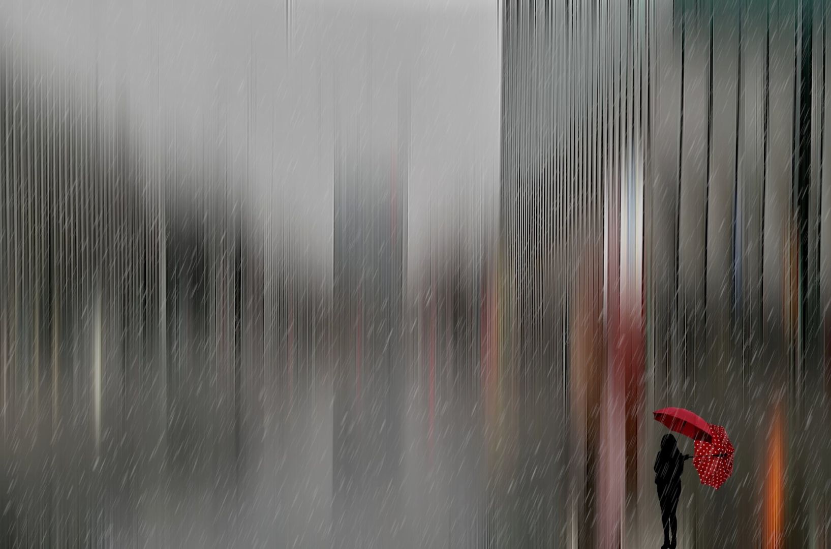 Es regnet ind der Stadt. Eine junge Frau mit einem roten Regenschirm steht am Straßenrand.
